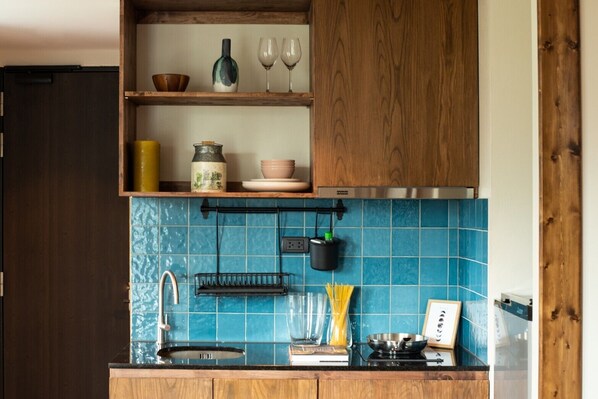 A kitchen with blue tiles, wooden cabinets, a stainless steel range hood, and various kitchen items on the countertop.