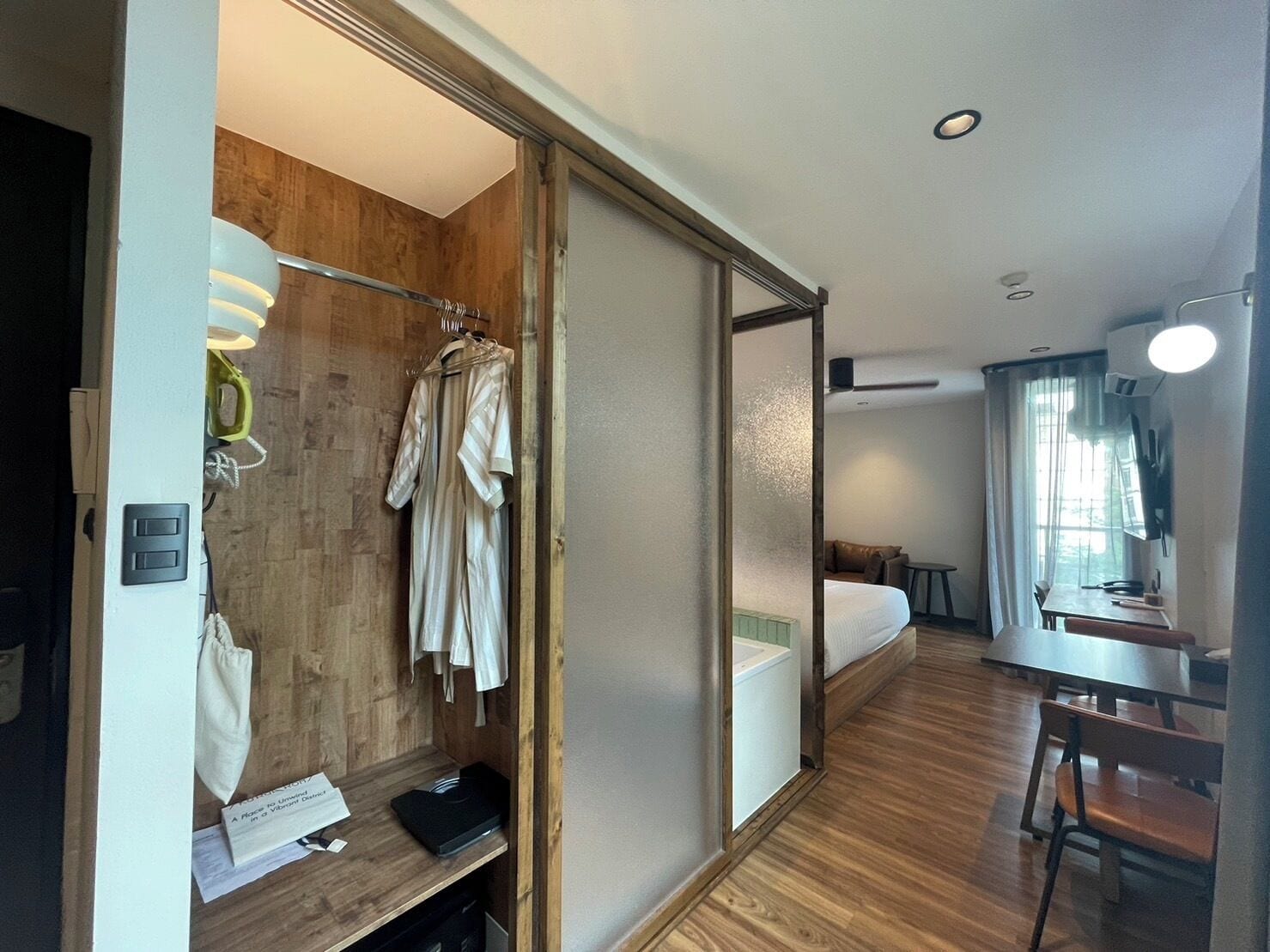A hotel room with a wooden wardrobe, a bed, a desk, and a chair.