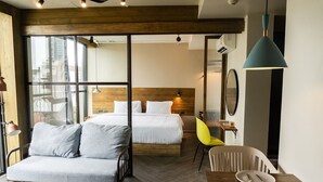 A modern hotel room with a bed, a sofa, a dining table with chairs, and a large window offering a view of the city. - Karaarom Hotel (Bangkok)