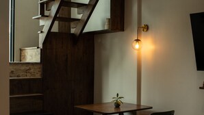 A modern interior with a wooden staircase, a table with a potted plant, and a wall-mounted light fixture. - Karaarom Hotel (Bangkok)