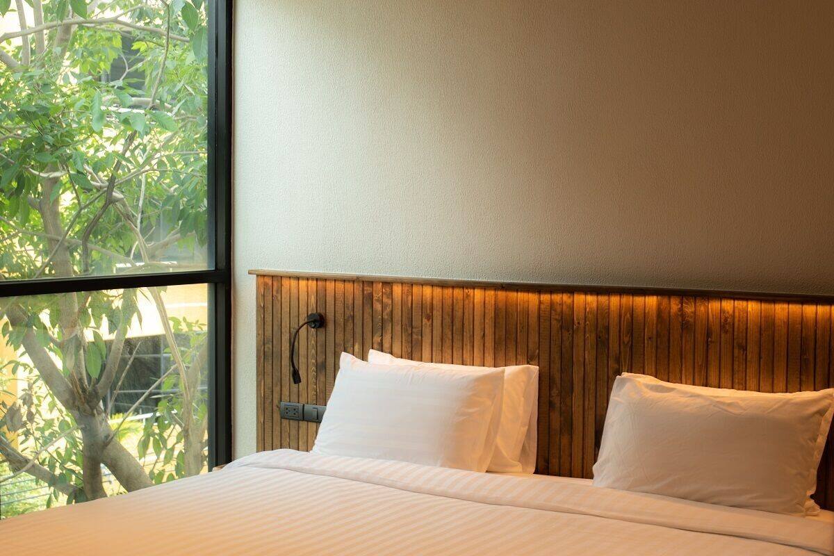 A hotel room with a large window, a wooden headboard, and a bed with white bedding.