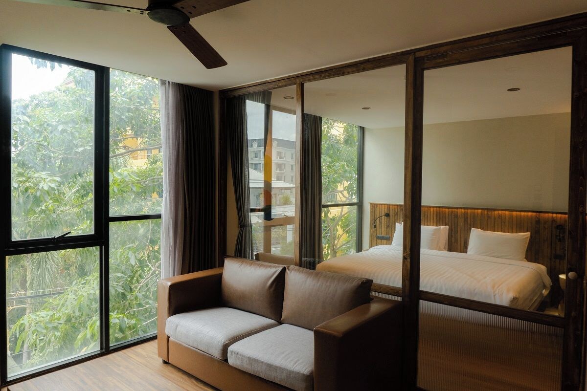 Una habitación de hotel moderna con un ventanal grande, un sofá, una cama y un cabecero de madera.