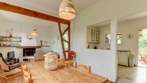 Un comedor espacioso con una mesa y sillas de madera, una chimenea y una cocina visible a través de un vano abierto.