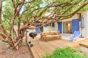 Een houten terras met een tafel, stoelen, een barbecue en een lounge stoel.