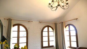A room with three arched windows, a chandelier, a bed with rolled towels, and a chair. - house swimming pool and jacuzzi sea view in the heart of olive trees
 (CAMPOROSSO)