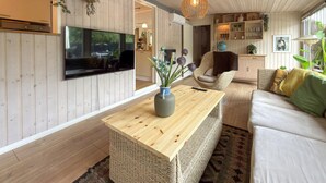 Una sala de estar moderna con piso de madera, un televisor montado en la pared, una mesa de centro de mimbre, un sofá y una estantería.