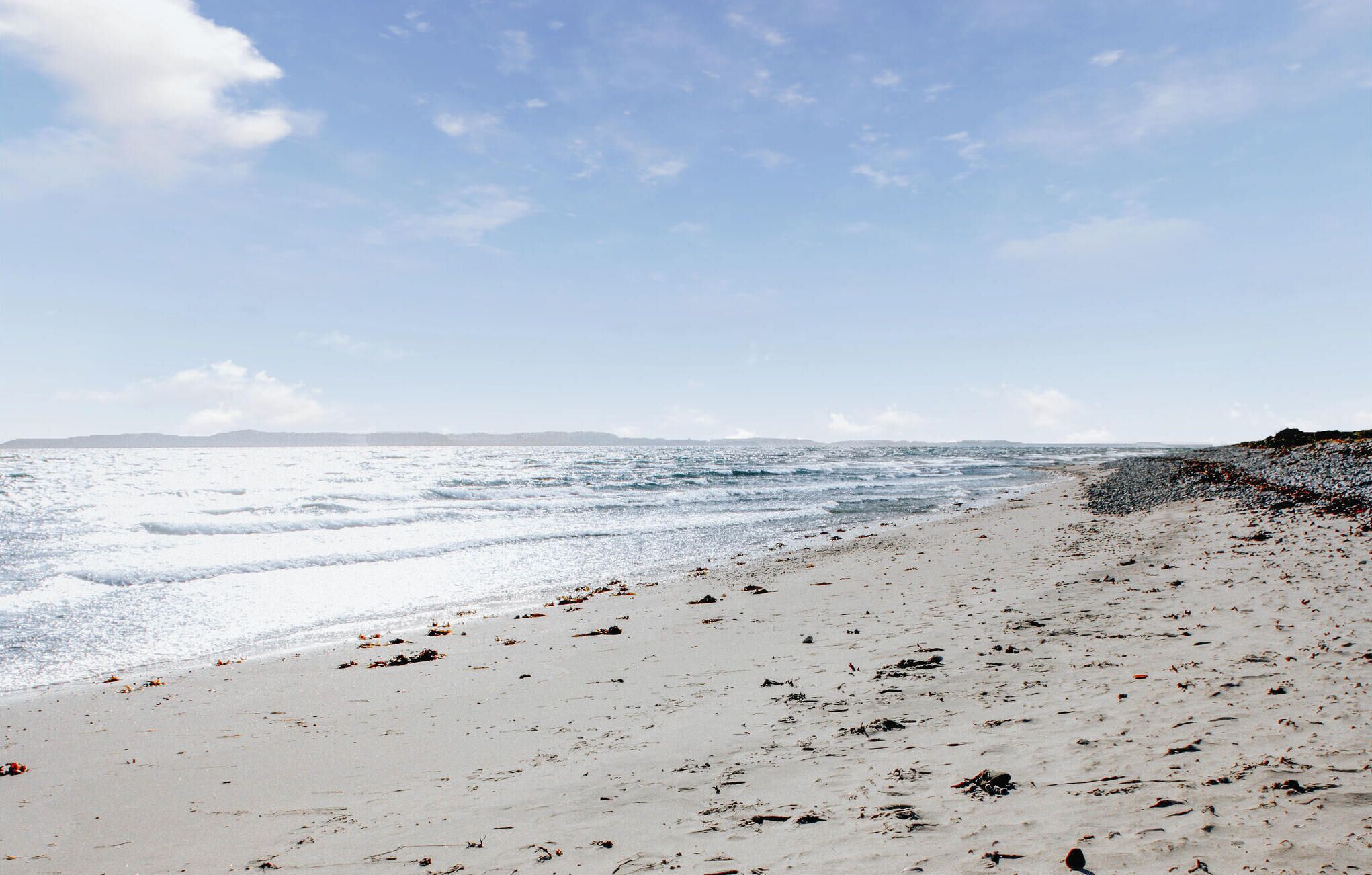 Une plage au rivage rocheux, où les vagues viennent se briser sur le sable.