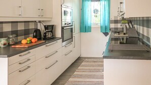 A compact kitchen with a coffee maker, oven, and a window with curtains.