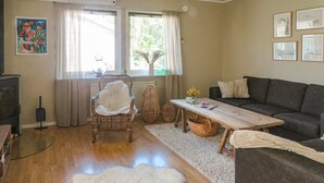 A living room with a sofa, a wooden coffee table, a chair with a white throw, a fluffy rug, and a painting on the wall.