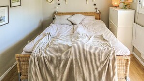 A neatly made bed with a striped blanket, a wicker headboard, and a bedside lamp.