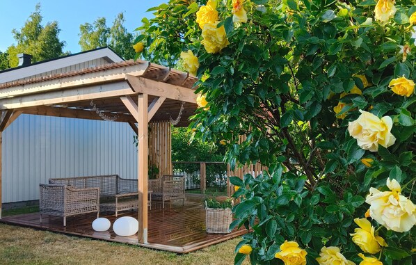 Relax in a serene garden setting with a pergola, wicker chairs, and a small table.