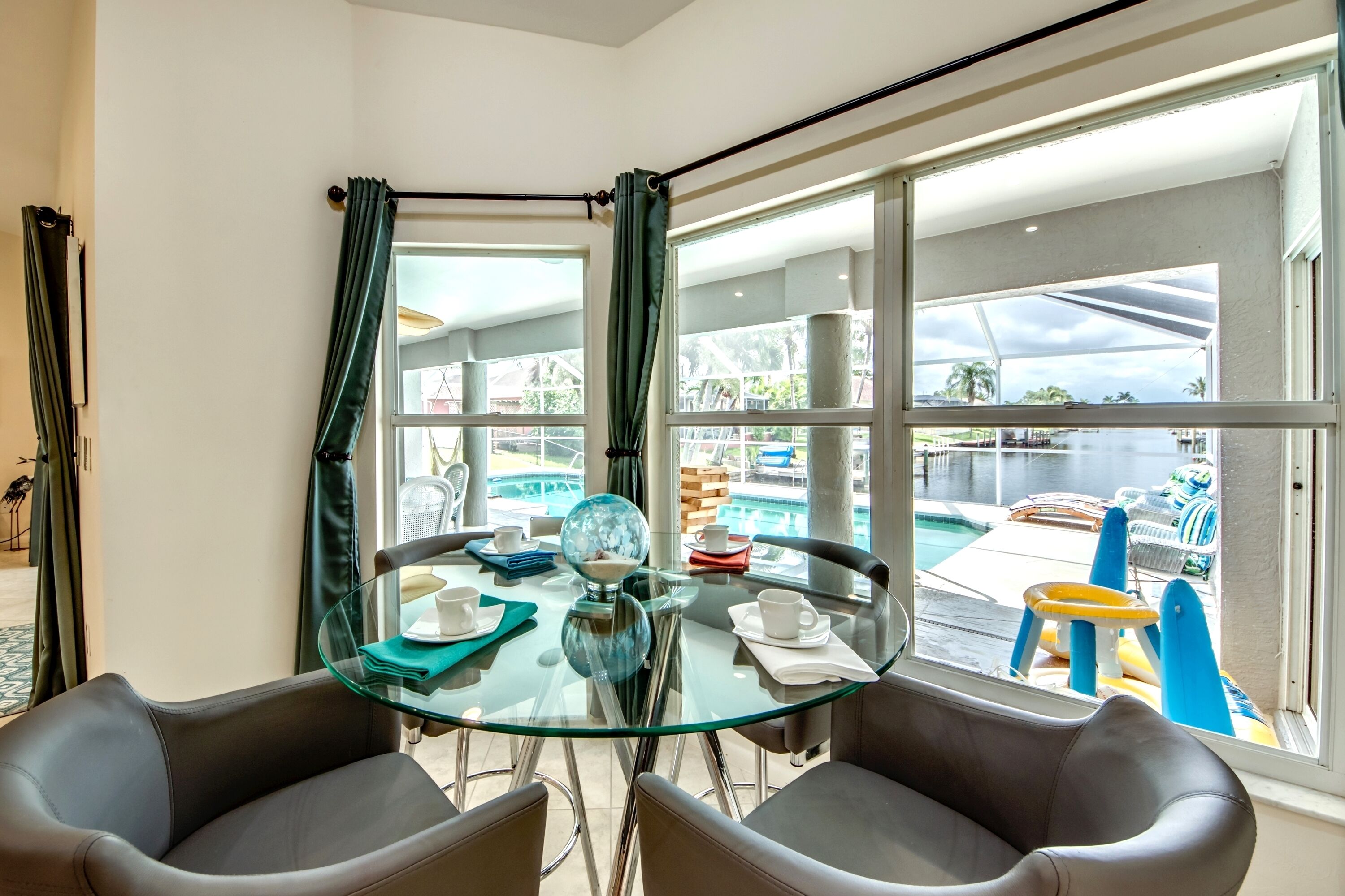 Habitación de esquina con una mesa de vidrio, dos sillones de cuero, un globo terráqueo y vistas a una piscina y zona exterior.