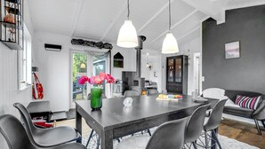 Uma área de jantar moderna com mesa de madeira escura, cadeiras cinzas e luminárias pendentes.
