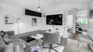 Uma sala de estar moderna com um sofá cinzento, uma mesa de centro, uma TV fixada na parede e um espaço de jantar com um banco.