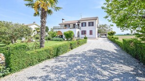 A two-story house with a gravel driveway leading to a white building with red shutters. - 2 bedroom cozy apartment in Grado (Grado)