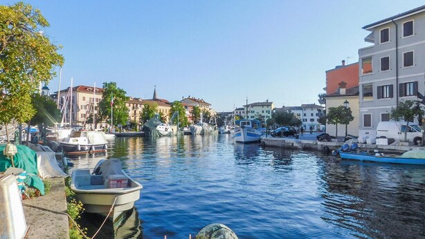 A canal with boats docked on both sides, surrounded by buildings with balconies and windows. - 2 bedroom cozy apartment in Grado (Grado)