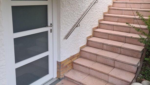 Eine Treppe mit Metallgeländer, die zu einer weißen Tür mit satinierten Glasscheiben führt.