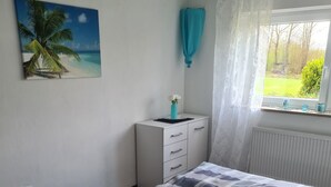 Ein Schlafzimmer mit Bett, Nachttisch, Fenster mit Vorhängen und einem Wandbild.