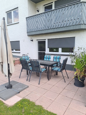 Un patio al aire libre con una mesa, sillas, una planta en maceta y un edificio con balcón.