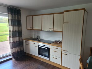 Una cocina compacta con armarios de madera, horno empotrado y ventana con cortinas.