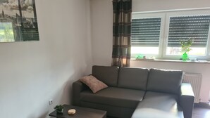 Ein modernes Wohnzimmer mit grauem Sofa, einem kleinen Couchtisch und einem Fenster mit Jalousien.