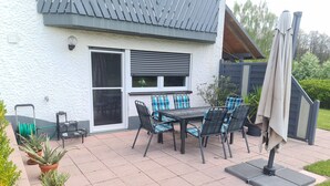 Eine Terrasse mit Tisch, Stühlen und Topfpflanzen, sowie eine Schiebetür.