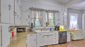 Una cocina con armarios blancos, encimera de granito, lavavajillas y una ventana con cortinas estampadas.