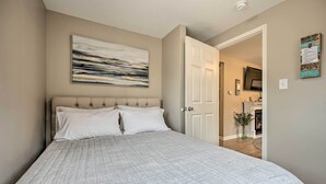Quarto com uma cama grande, um quadro abstrato na parede e uma porta que dá para um corredor.