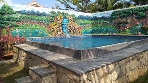 Una piscina con un mural decorativo en las paredes, rodeada de escalones de piedra y un muro de piedra.