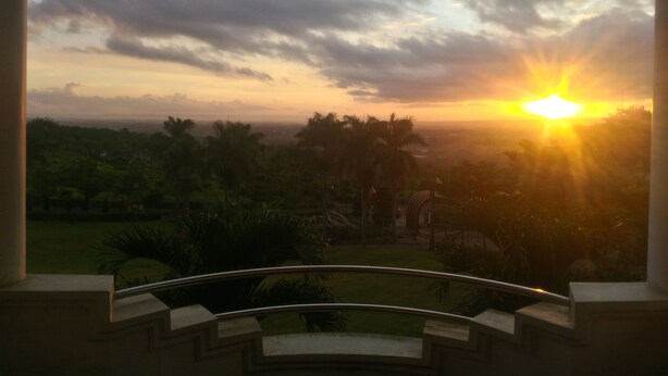 Un balcón con vista a un atardecer sobre un paisaje de palmeras.