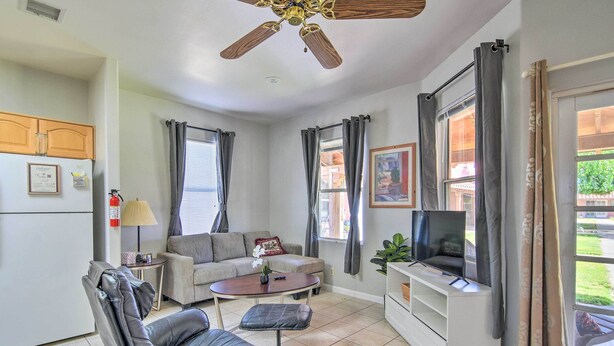 A compact living space with a ceiling fan, a sofa, a coffee table, a TV on a stand, and a kitchen area with a refrigerator and cabinets. - 'Best Night's Sleep' Apt Near Skydive Arizona (Eloy)