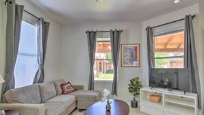 A living room with a sofa, a coffee table with a flower vase, a TV on a white stand, and curtains on the windows. - 'Best Night's Sleep' Apt Near Skydive Arizona (Eloy)