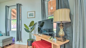 Ein Wohnzimmer mit Fernseher, Lampe, Sofa, Blumentopf und einem Fenster mit Vorhängen.