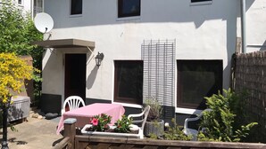 A two-story house with a balcony, a satellite dish, and a small garden area with potted plants and a table.