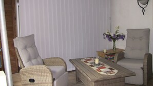 A room with two wicker chairs, a small table with a candle, and a vase with flowers.