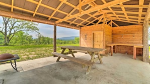 A rustic wooden structure with a picnic table and benches, surrounded by a concrete floor and a view of greenery. - Updated Studio Cabin in Ozark w/ Yard & Mtn View (Ozark)