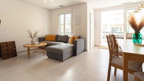 Een moderne woonkamer met een grijze modulaire bank, een ronde houten tafel, en een eethoek met houten stoelen.