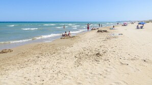 Een zandstrand met mensen, sommigen zitten en anderen staan, en enkele parasols.