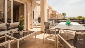 Een terras met een bank, een glazen tafel en stoelen. Achtergrond is het stadsbeeld en palmbomen.