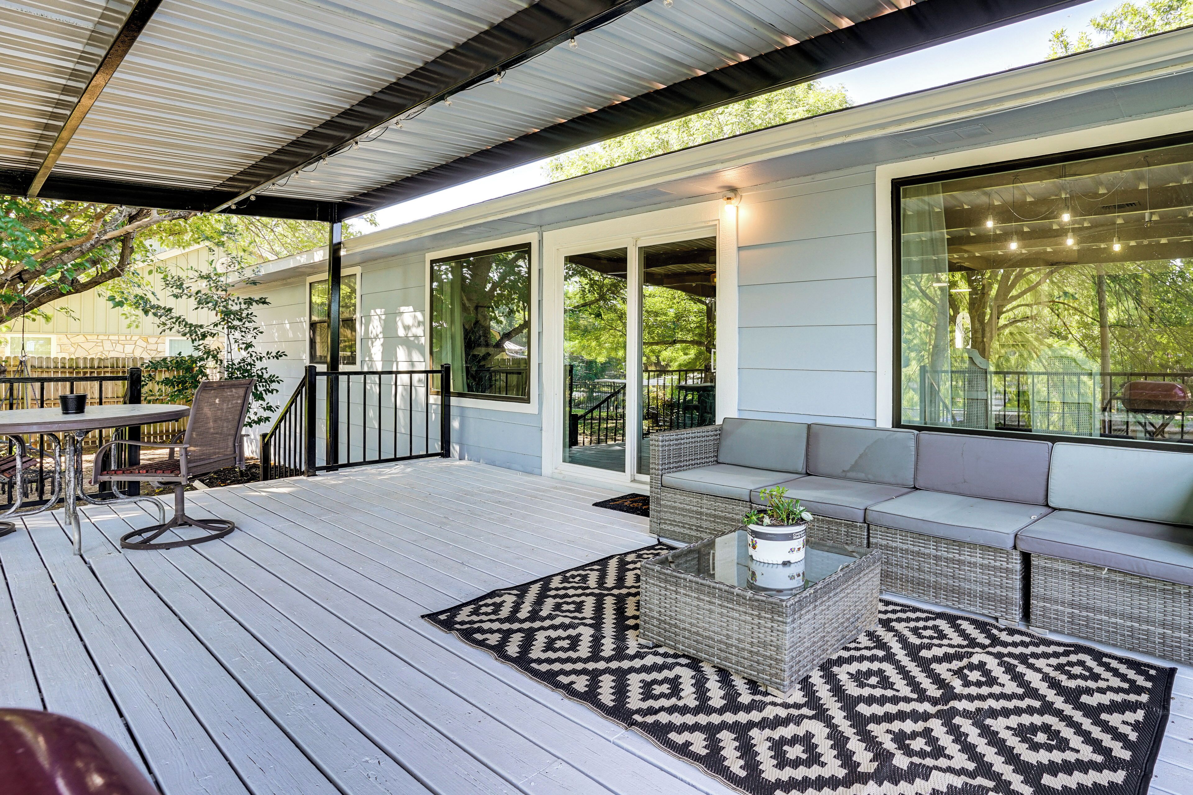 A covered outdoor patio with a seating area, a table, and a patterned rug.