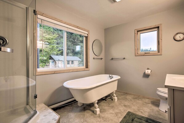 A bathroom with a freestanding bathtub, a toilet, a window, and a mirror.