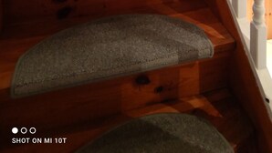 Eine Holztreppe mit weißen Balustraden und Blick auf einen Küchenbereich im Hintergrund.