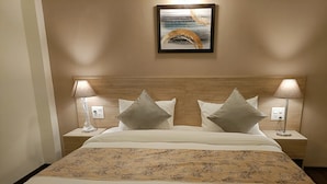 A neatly made bed with a patterned bedspread, two bedside lamps, and a framed picture on the wall. - STARLIT SUITES SHIRDI (Rahata)
