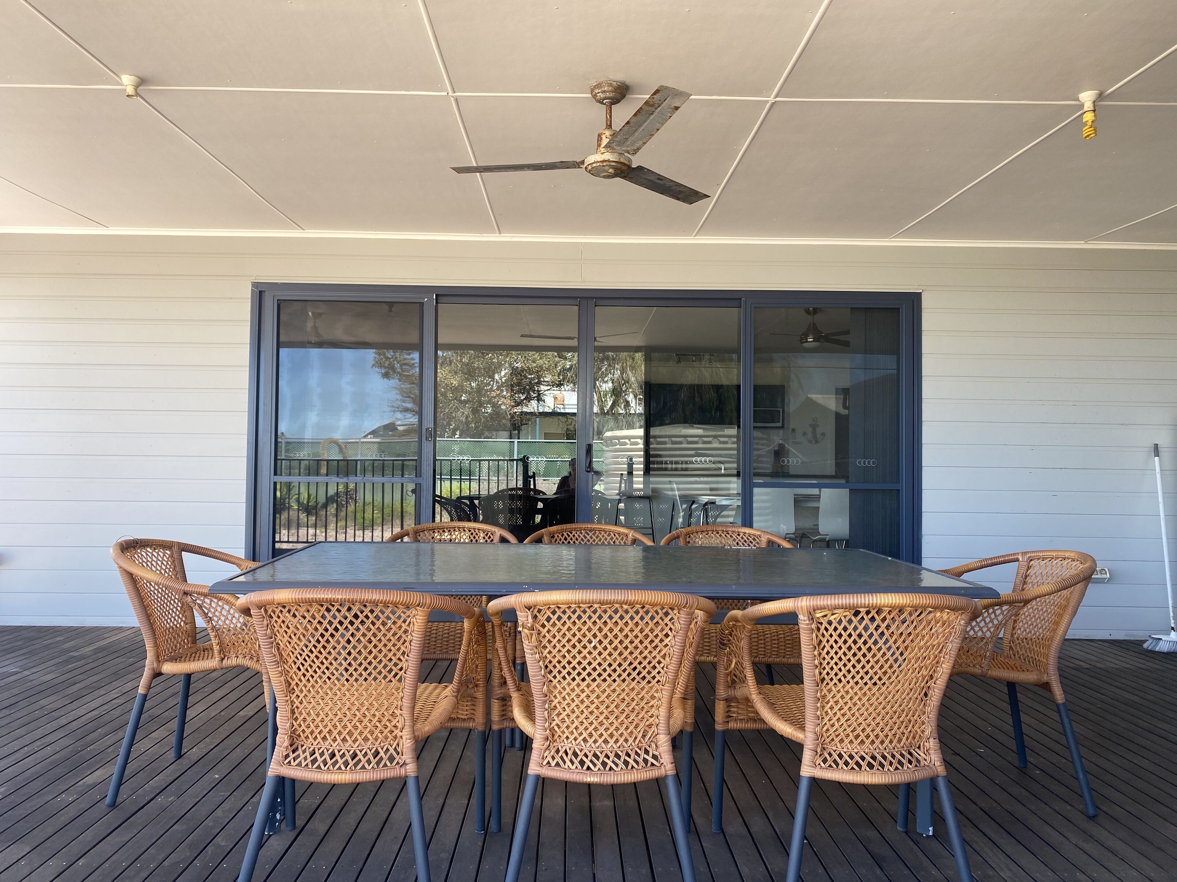 An outdoor patio with a table and chairs, a ceiling fan, and a view through a glass door.