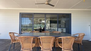 Eine Terrasse im Freien mit Tisch und Stühlen, einem Deckenventilator und Blick durch eine Glastür.