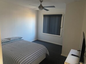 A bedroom with a bed, a ceiling fan, a window with blinds, and a television on a stand. - Relax and enjoy the beach air. 2 mins walk to the beach. (North Beach)