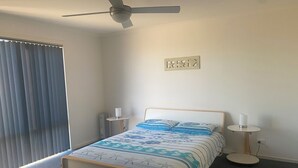 Ein Schlafzimmer mit Bett, Deckenventilator, Heizkörper und einem Fenster mit Jalousien.