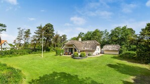 A thatched-roof house with a well-maintained lawn and a small garden area.