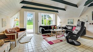 A spacious living room with a high ceiling, a black leather sofa, a black leather armchair, a small round table, and a plaid-patterned sofa.