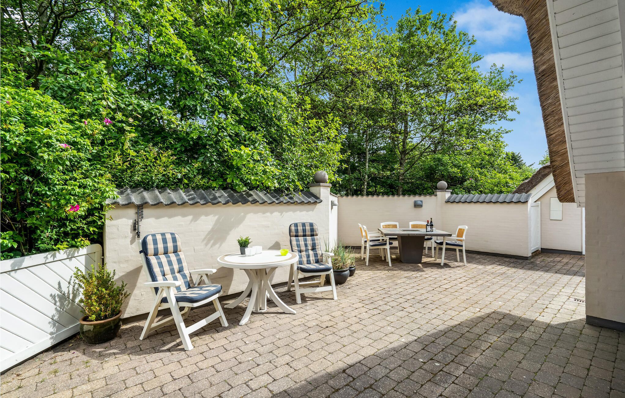 A patio with a table and chairs, surrounded by a white wall and a tiled roof.